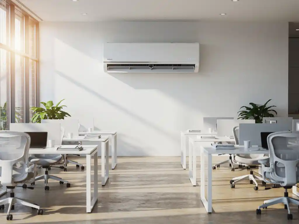Wandgemonteerde split-airco boven een moderne open kantoorruimte met ergonomische bureaustoelen en natuurlijk lichtinval.