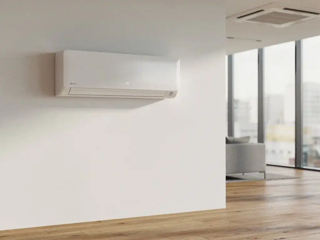 Wandgemonteerde airconditioning in modern kantoor met witte muren, houten vloer en grote ramen die daglicht doorlaten.